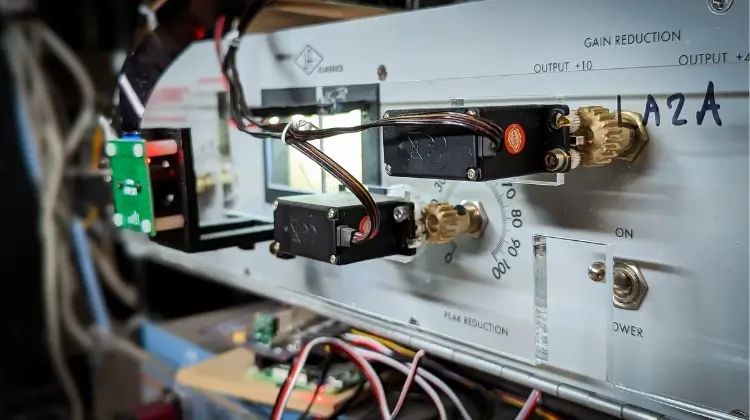 Access Analog's robotic actuators mounted on a real LA-2A in the rack, with brass gears engaging the Peak Reduction and meter selector controls so they can be turned remotely from a DAW. The unit is hand-labelled LA2A.