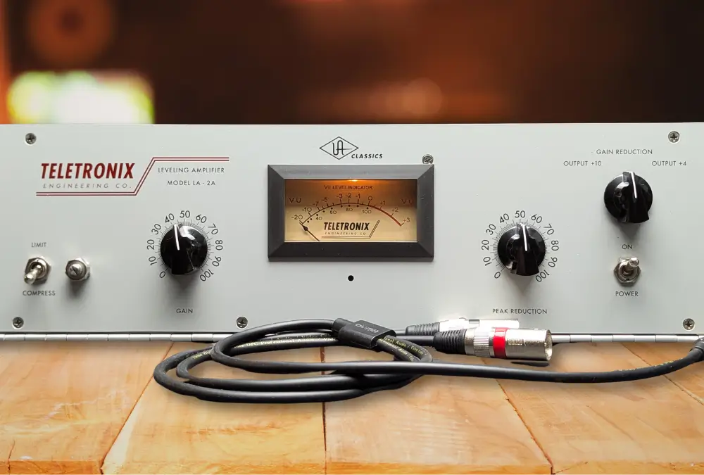 A Teletronix LA-2A Leveling Amplifier photographed head-on, showing its two large control knobs marked 0 to 100 (Gain on the left, Peak Reduction on the right), the centre VU meter, the Limit/Compress toggle, and the meter selector switch.